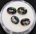 Stylized promotional image of four oval-cut mystic topaz gemstones, subdued rainbow colors